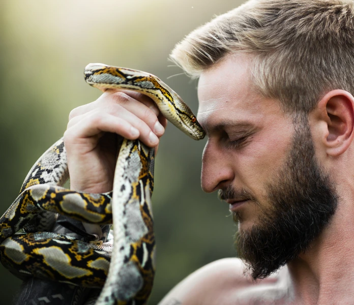 Zdeněk sedící na lávce v rákosí s hadem kolem krku